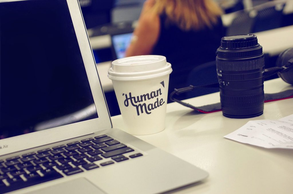 Open MabBook next to a white coffee cup with dark Human Made branding