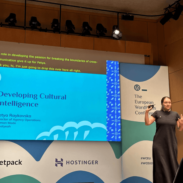 Petya Raykovska on stage delivering a talk with a screen showing slides behind her